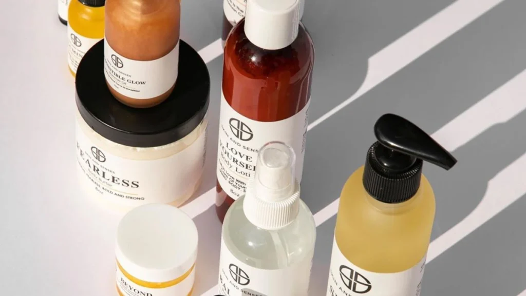 Assorted waterless beauty product bottles and jars with white labels arranged on a white surface casting shadows.