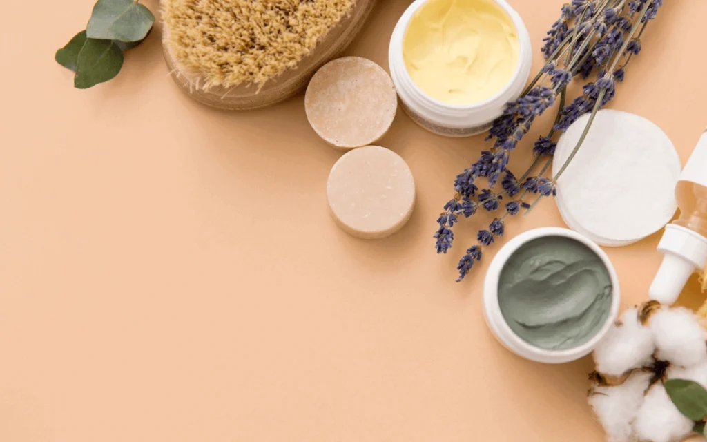 Natural skincare items including creams, solid bars, a brush, lavender, and cotton on a beige background.