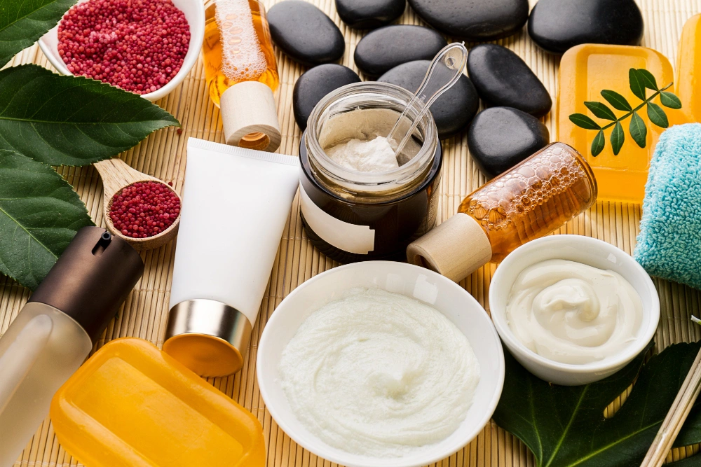 Assorted full body care products including creams, oils, soap bars, and natural elements on a bamboo mat background.
