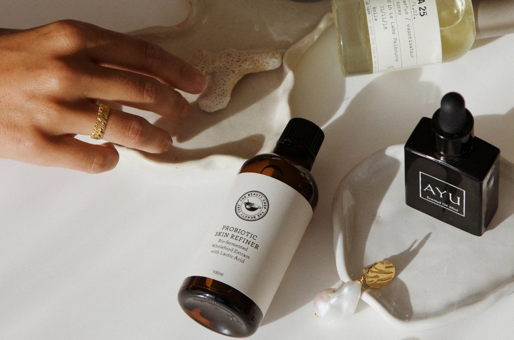 Probiotic Cosmetics: 7 Proven Benefits for a Superior Skin Microbiome 8 A hand reaches toward probiotic skincare bottles and jewelry displayed on a white surface with soft shadows.