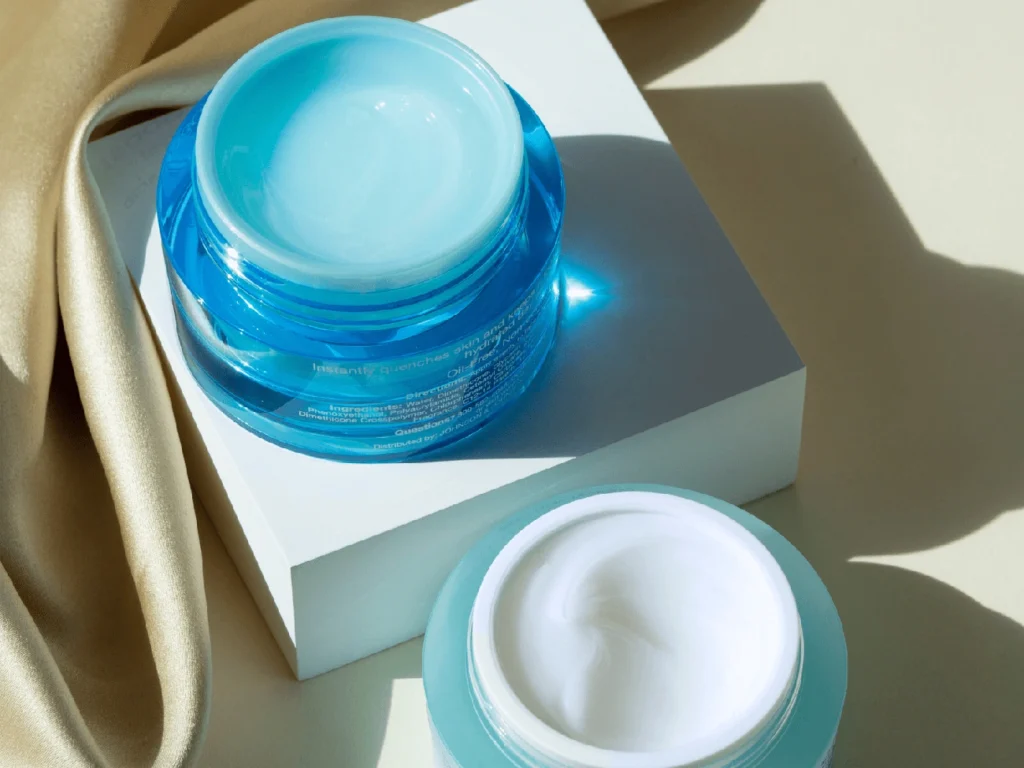 Barrier-First Creams: 7 Proven Ingredient Standards for Superior Dermal Repair 8 Two open skincare cream jars, one blue and one white, placed on a white block with beige fabric nearby.